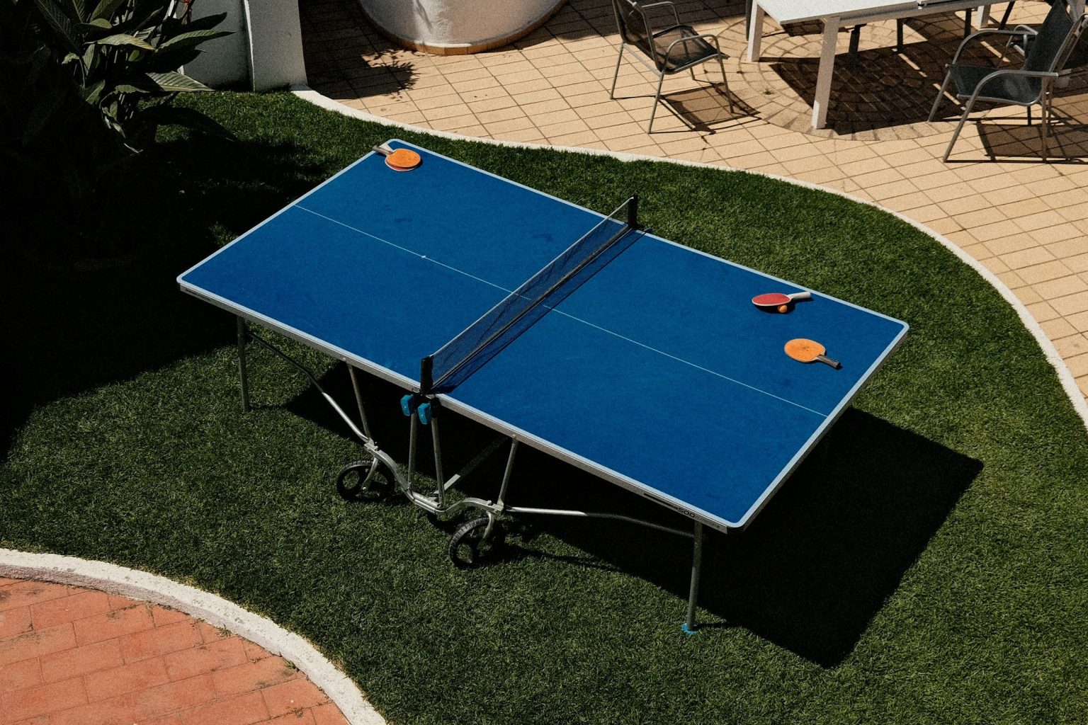Table de ping-pong Pongori d’extérieur bleue, dépliée sur une pelouse avec raquettes et balle